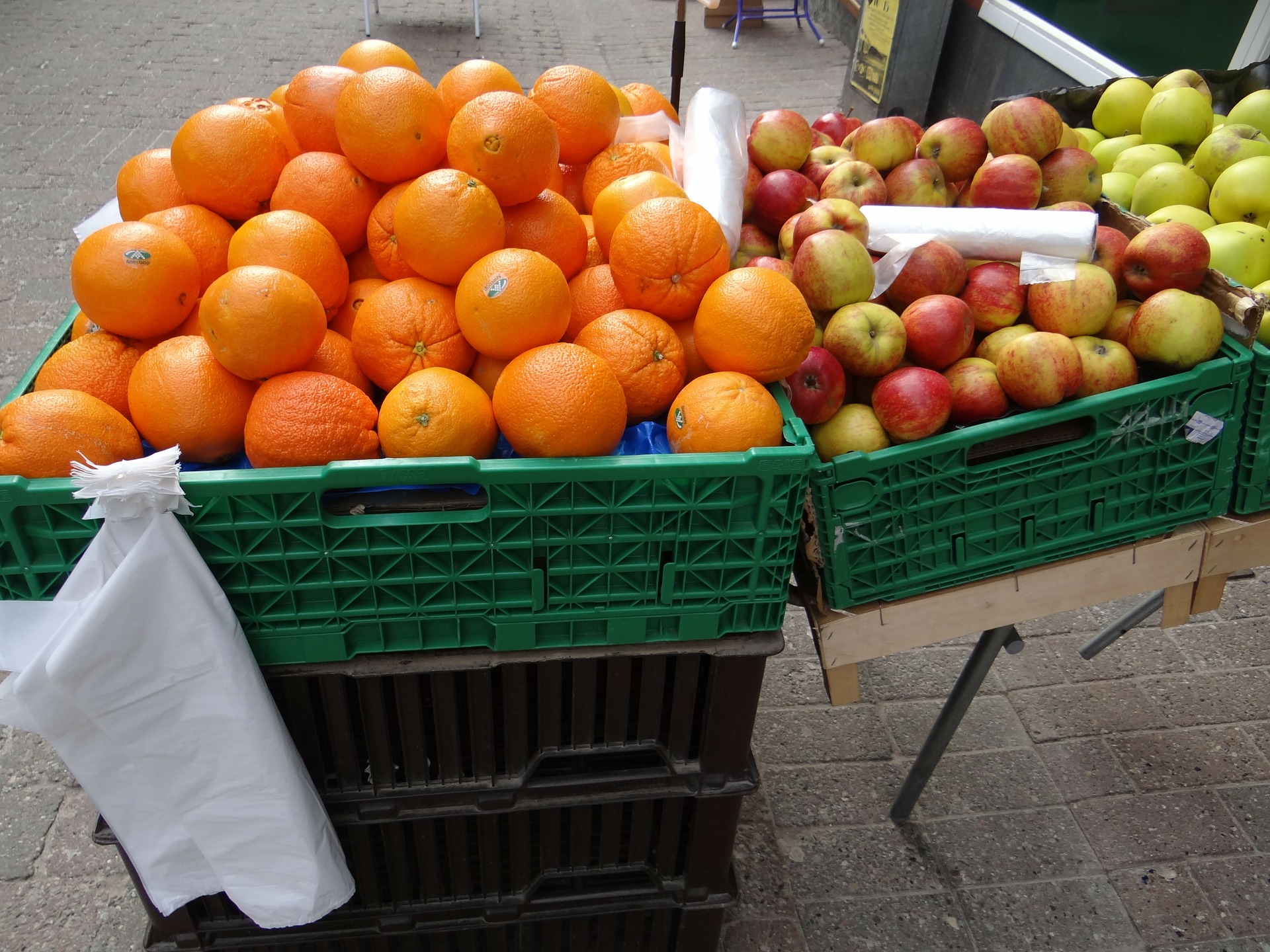 Oranges, apples, and pears in green bins, with plastic produce bags tied to the bins.